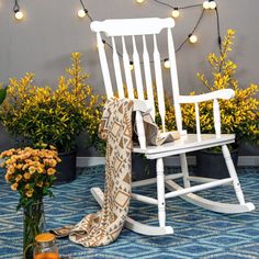 a white rocking chair sitting on top of a blue rug next to potted plants