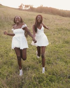 two young women in white dresses are running through the grass holding hands with each other