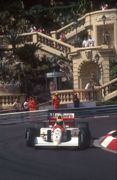 a man driving a race car down a street next to a tall building with stairs