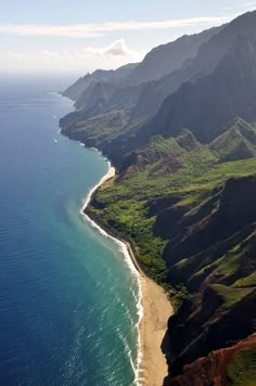 an aerial view of the ocean and mountains near a sandy beach with green grass on both sides