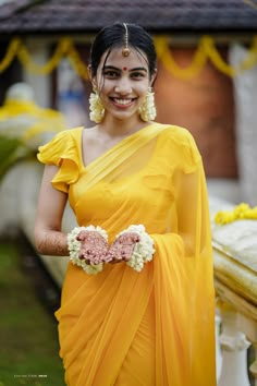 a woman in a yellow sari with flowers around her waist and smiling at the camera