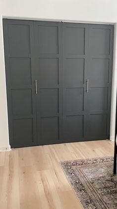 an empty room with black doors and wood flooring on the walls, along with a rug in front of it