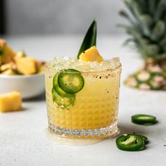 a pineapple and cucumber cocktail with limes on the side, surrounded by sliced jalapenos