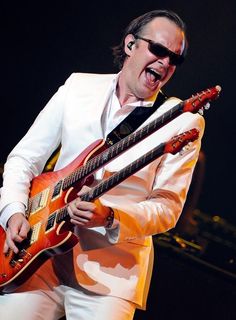 a man in white suit playing an electric guitar on stage with his mouth open and tongue out