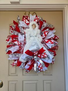 a red and white christmas wreath with a doll hanging from it's front door