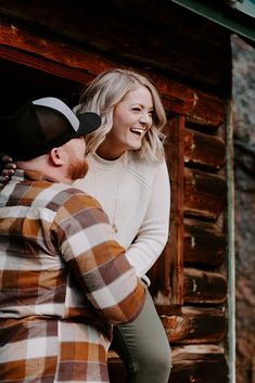 a man and woman standing next to each other in front of a log cabin smiling