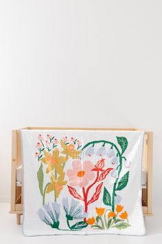 a white blanket with colorful flowers on it in front of a wooden crib against a wall