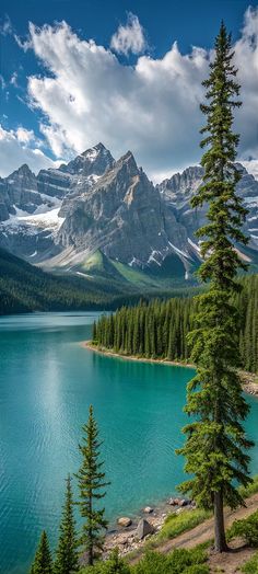 the mountains are covered in snow and green pine trees near a lake with clear blue water