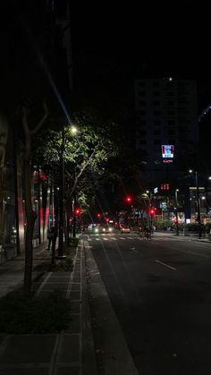 an empty city street at night with red traffic lights and tall buildings in the background