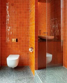 an orange tiled bathroom with two toilets and a sink