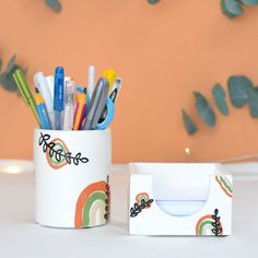 a cup that has some pens and pencils in it next to a cardboard box