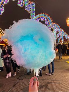 a person holding up a blue and white lollipop in front of an amusement park