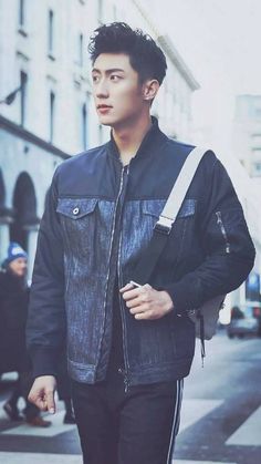 a young man walking down the street wearing a black jacket and carrying a white bag