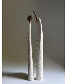 two tall white vases sitting next to each other on top of a gray surface