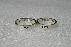 two silver rings with hearts and words on them sitting on a white surface, one has the word love written in cursive writing