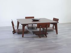 a wooden table with four chairs and a bowl on it's end, in front of a white wall