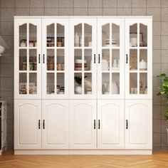 a large white cabinet with glass doors in a room next to a potted plant