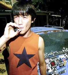 a young man standing in front of a parked car while talking on a cell phone