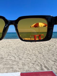 a pair of sunglasses sitting on top of a sandy beach next to an orange umbrella