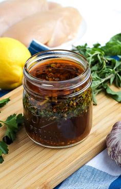 a wooden cutting board topped with a jar of pickles and herbs next to lemons