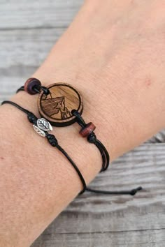 a person wearing a bracelet with a wooden disc and two charms on it's wrist