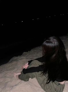 a woman sitting in the sand at night with her back turned to the camera,