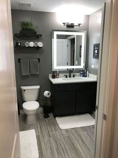 a bathroom with gray walls and wood floors, white toilet and black vanity mirror above the sink