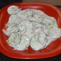 a red plate topped with cucumbers and sauce on top of a countertop