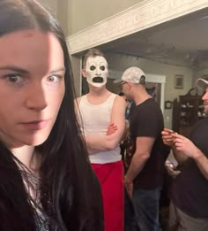 a group of people standing in a room with one person wearing a mask and the other looking at the camera