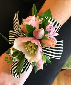 a woman's wrist is adorned with pink flowers and greenery, along with black and white striped ribbon