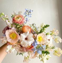 a person holding a bouquet of flowers in their hand with white, pink and blue flowers