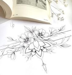 an open book sitting on top of a table next to a flower tattoo design,