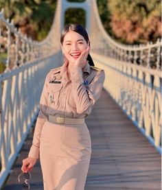 a woman in uniform standing on a bridge with her hand to her face and looking at the camera