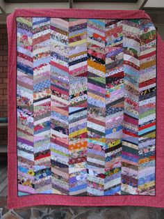 a pink quilt hanging from the side of a building with lots of different colored strips on it