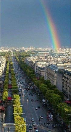 a rainbow in the sky over a city with tall buildings and cars driving down it