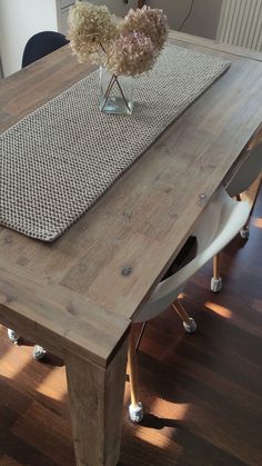 a wooden table with some flowers in a glass vase on it and a placemat