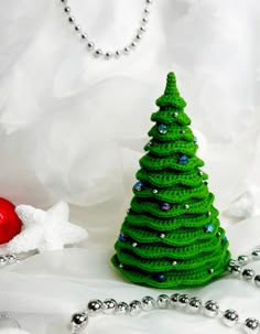 a crocheted christmas tree sitting next to a beaded necklace on a white background