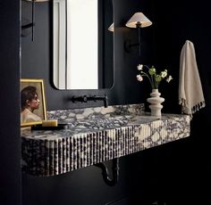 a bathroom with black walls and marble counter top, white vases on the sink