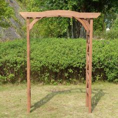 a wooden arbor in the middle of a grassy area with bushes and trees behind it