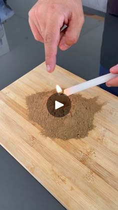 a person lighting a candle in the middle of a wooden cutting board with dirt on it