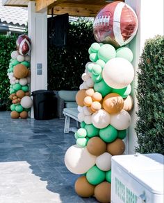 balloons and footballs are hanging from the side of a building in front of bushes