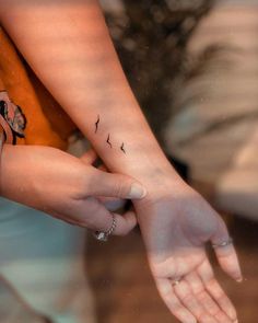 two people holding hands with small birds on their wrist tattooing one another's hand