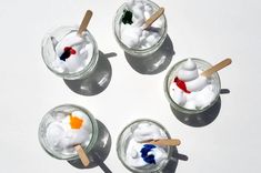 four small jars with marshmallows and toothpicks in them on a white surface