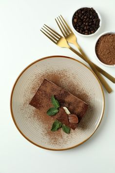 a white plate topped with chocolate cake next to two bowls of cocoa and coffee beans