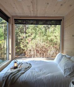 a bed with white sheets and pillows in front of a window that looks out onto the woods