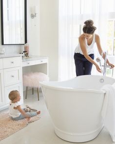 a woman and her baby are playing in the bathtub while another child sits on the floor