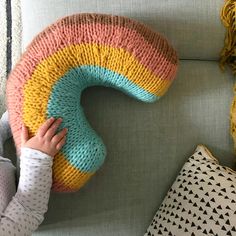 a child is playing with a knitted rainbow pillow on a couch next to pillows