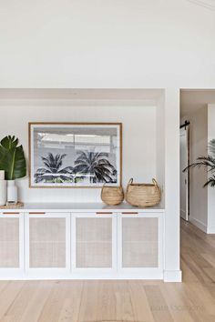 a living room with white walls and wooden floors, two baskets on top of the shelf