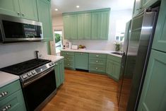 a kitchen with green cabinets and white counter tops, wood flooring and stainless steel appliances