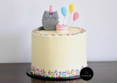 a birthday cake with a cat on top and balloons sticking out of the icing